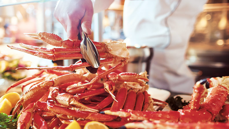 grabbing crab legs off a buffet with tongs